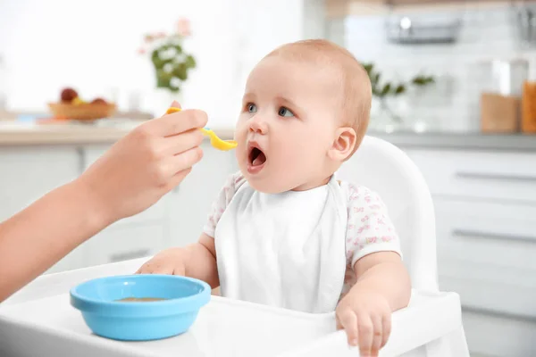 Moeder voeding baby met lepel in keuken — Stockfoto