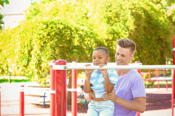 Junger Vater mit adoptiertem afrikanisch-amerikanischem Jungen auf dem Sportplatz — Stockfoto