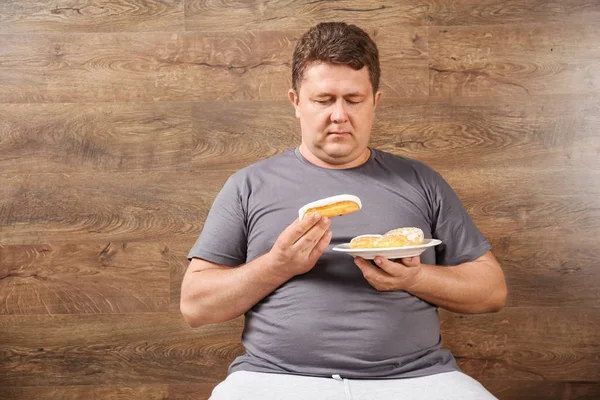 Overgewicht jongeman eten snoep op houten achtergrond — Stockfoto