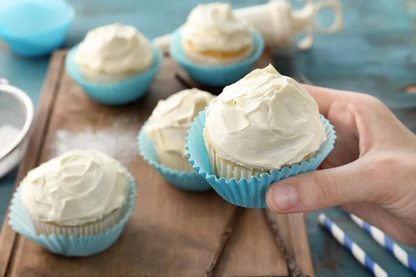 Mujer sosteniendo sabroso cupcake de vainilla sobre fondo borroso — Foto de Stock