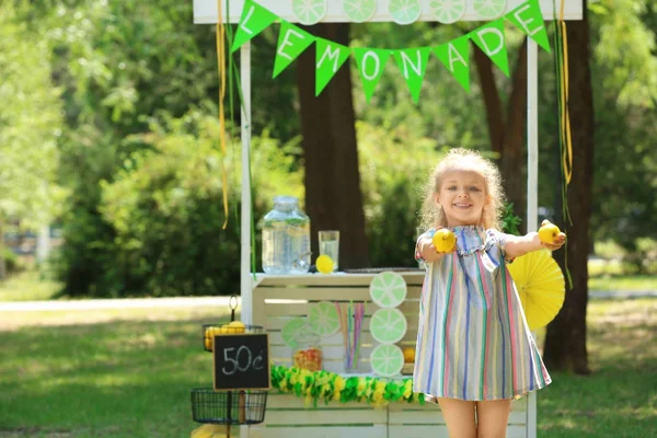 Schattige lachende meisje met citroenen in de buurt van limonade staan in park — Stockfoto