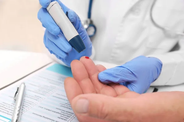Técnico médico em luvas de látex recolhendo amostra de sangue de paciente com caneta lancet no hospital — Fotografia de Stock