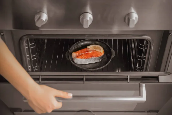 Женщина закрывает духовку стейком лосося — стоковое фото