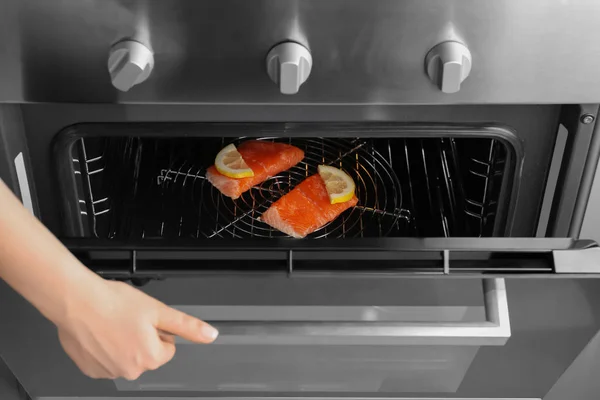 Vrouw sluiten oven met plakjes rode visfilet binnen — Stockfoto