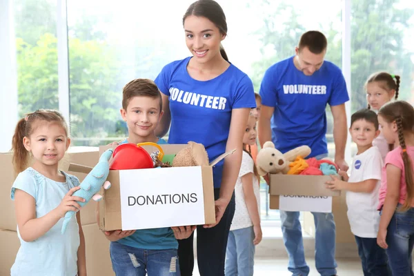 Happy volunteers with children holding donation boxes indoors — Stock Photo, Image