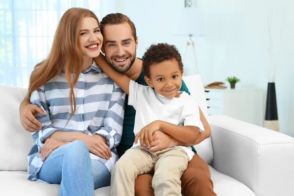 幸福的情侣，与领养非洲裔美国人的孩子坐在沙发上在家里 — 图库照片