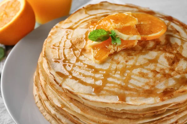 Montón de panqueques finos servidos con miel y rodajas de naranja en un plato blanco — Foto de Stock