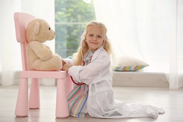 Meisje met medische vacht spelen met teddybeer en stethoscoop op verdieping — Stockfoto