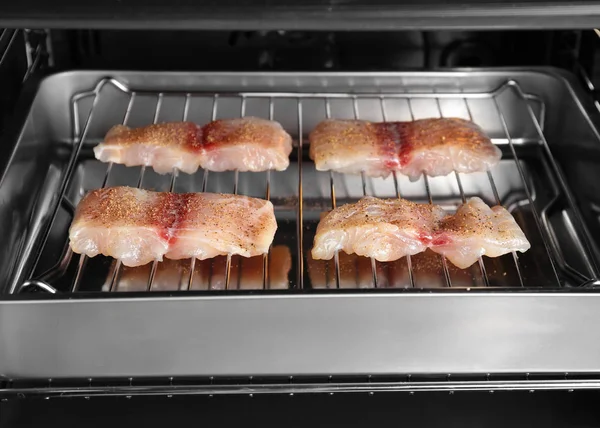 Raw slices of fish fillet on roasting pan in oven — Stock Photo, Image