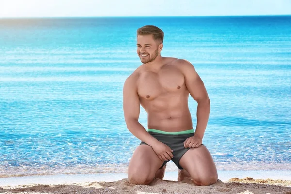 Giovane bell'uomo in posa sulla spiaggia vicino al mare blu — Foto Stock