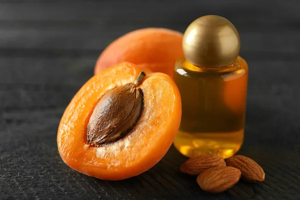 Láhev meruňkový olej s čerstvým ovocem a jádra na dřevěný stůl — Stock fotografie