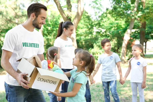 Jóvenes voluntarios y niños con caja de donaciones al aire libre —  Fotos de Stock