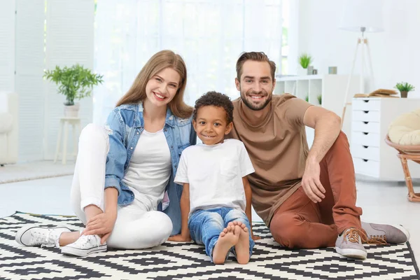 Couple heureux avec adopté afro-américain garçon assis sur le tapis à la maison — Photo