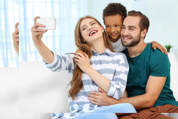 Szczęśliwa para z przyjętych African-American chłopak biorąc selfie na kanapie w domu — Zdjęcie stockowe