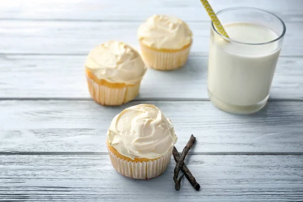 Cupcakes de baunilha saborosos e copo de leite na mesa de madeira — Fotografia de Stock