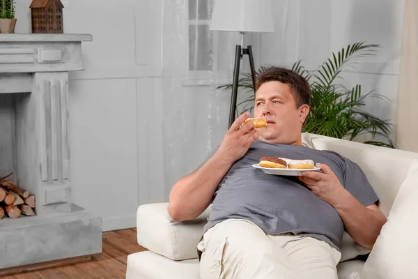 Genç adam yeme tatlılar kanepe evde kilolu — Stok fotoğraf