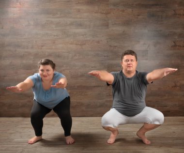Overweight couple training together against wooden wall clipart