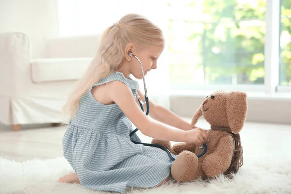 Menina brincando com coelho e estetoscópio no chão — Fotografia de Stock