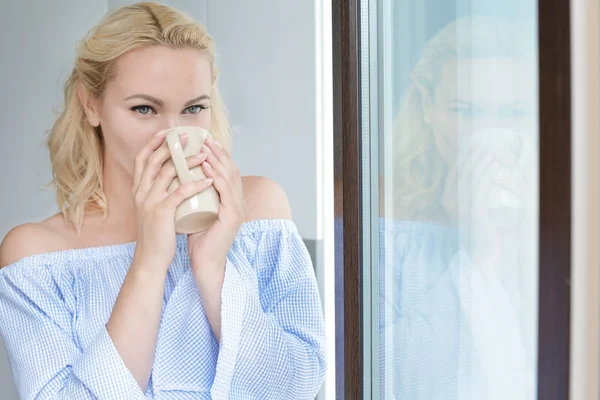 Schöne Frau mit Kaffee steht am Fenster zu Hause — Stockfoto