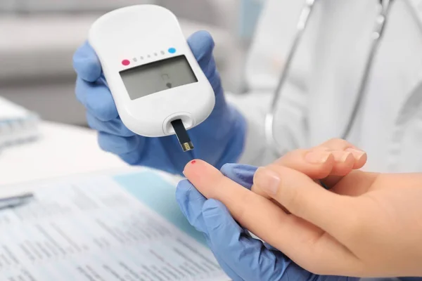 Técnico médico en guantes de látex que evalúa el nivel de glucosa del paciente con glucosímetro digital en el hospital —  Fotos de Stock