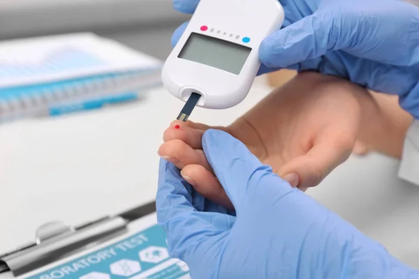 Técnico médico en guantes de látex que evalúa el nivel de glucosa del paciente con glucosímetro digital en el hospital — Foto de Stock