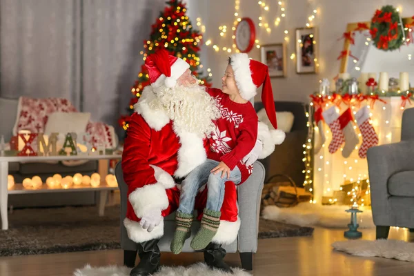 Ragazzino felice seduto sulle ginocchia di Babbo Natale in camera con belle decorazioni natalizie — Foto Stock