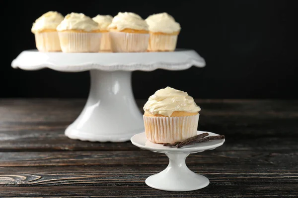 Tasty vanilla cupcakes on wooden table against black background — Stock Photo, Image