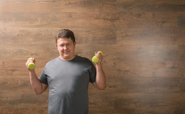 Overweight man with dumbbells on wooden background — Stock Photo, Image