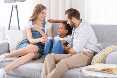 Mutlu çift evde kanepede oturan kabul edilen Afrikalı-Amerikalı çocuk ile