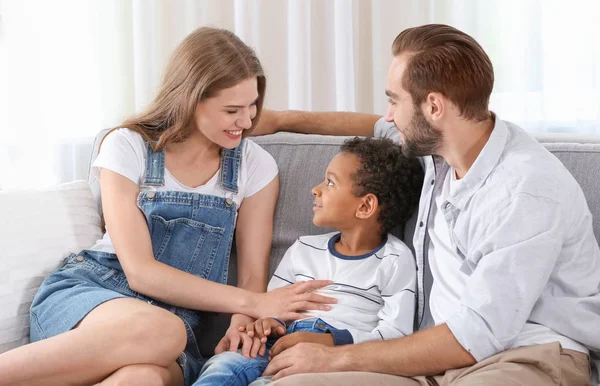 Casal feliz com o menino afro-americano adotado sentado no sofá em casa — Fotografia de Stock