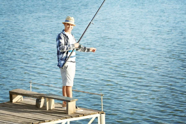 Young man fishing from pier on river — Stock Photo, Image