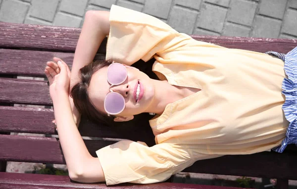 Schöne junge Frau auf Bank liegend an sonnigem Tag — Stockfoto