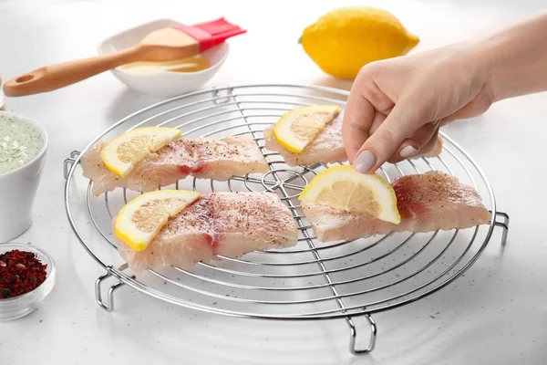 Женщина добавляет ломтики лимона к рыбному филе на белый стол — стоковое фото