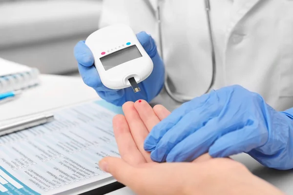 Técnico médico en guantes de látex que evalúa el nivel de glucosa del paciente con glucosímetro digital en el hospital —  Fotos de Stock