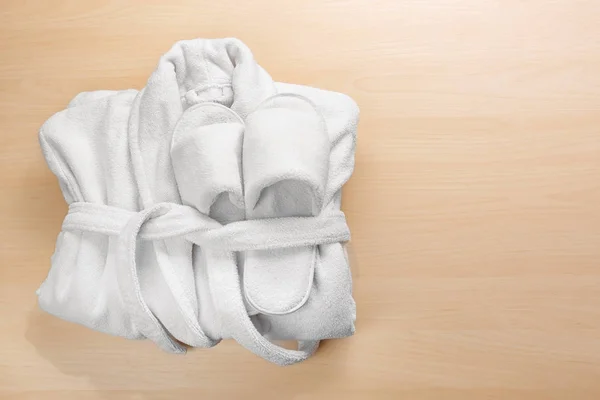Διπλωμένο λευκό μπουρνούζι και spa παντόφλες σε φόντο ξύλινη — Φωτογραφία Αρχείου