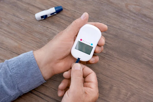 Man holding digital glucometer on wooden background — Stock Photo, Image