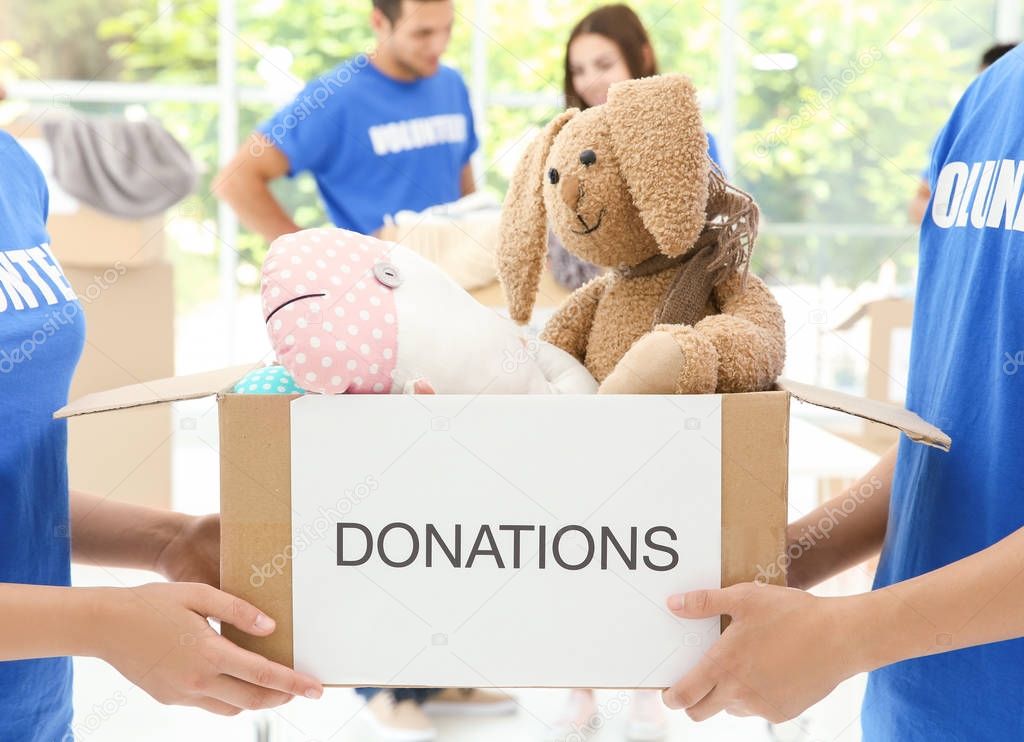 Two volunteers holding box with donated toys indoors