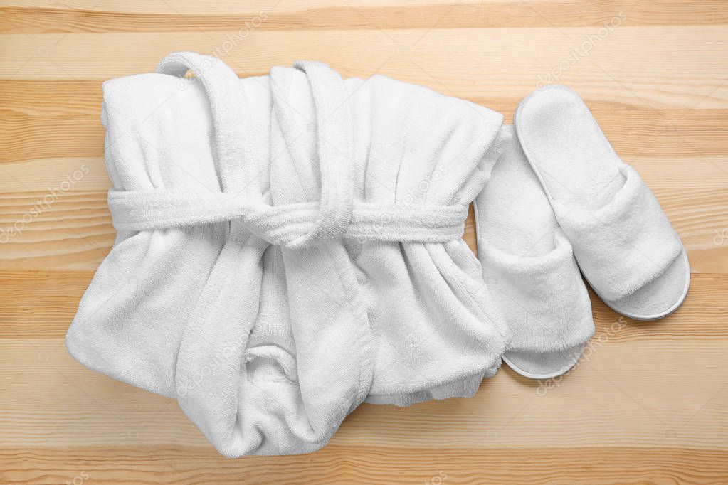 Folded white bathrobe and spa slippers on wooden background