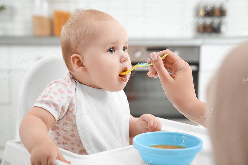 Mother feeding baby with spoon in kitchen