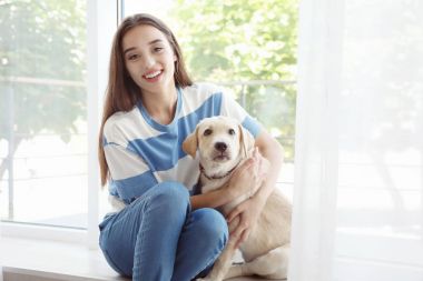 Pencere yakınındaki sarı av köpeği ile oturan genç kadın
