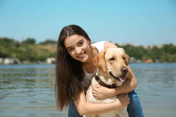 Mujer joven descansando con amarillo retriever cerca del río — Foto de Stock