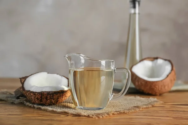 Ripe coconut and pitcher with oil on wooden table — Stock Photo, Image