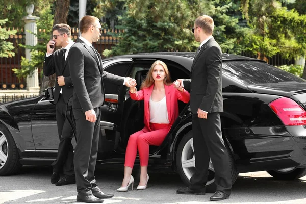Lijfwachten helpen jonge zakenvrouw om uit auto — Stockfoto
