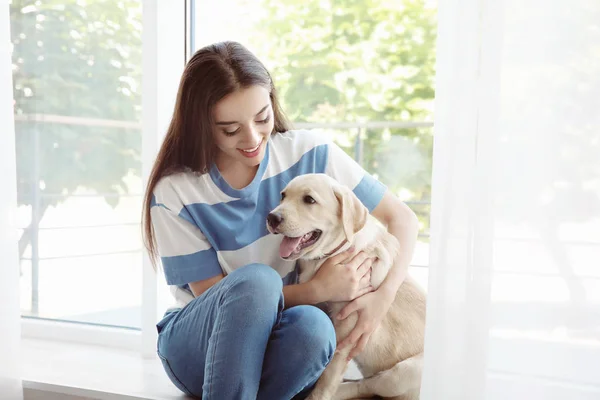 Mujer joven sentada con amarillo retriever cerca de la ventana — Foto de Stock