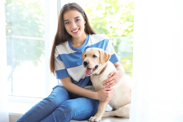 Ung kvinna sitter med gula retriever nära fönster — Stockfoto