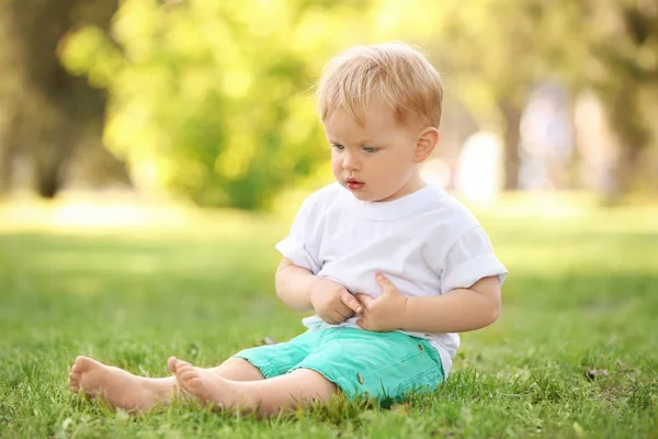 Ładny chłopczyk siedzi na zielonej trawie w parku — Zdjęcie stockowe