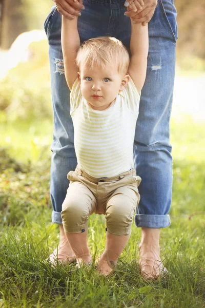 Mother and cute baby boy walking on green grass in park Stock Picture