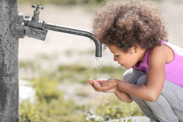 Un enfant afro-américain boit de l'eau du robinet dehors. Concept de pénurie d'eau — Photo