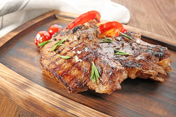 Tasty grilled steaks with vegetables on wooden board