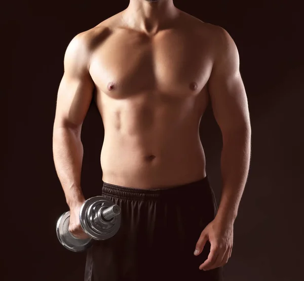 Sporty young man with dumbbell on dark background — Stock Photo, Image